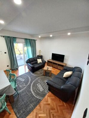 A living room with a sofa, a television, a dining area with a table and chairs, and a window with curtains. - Apartment Snjezana (Senj)