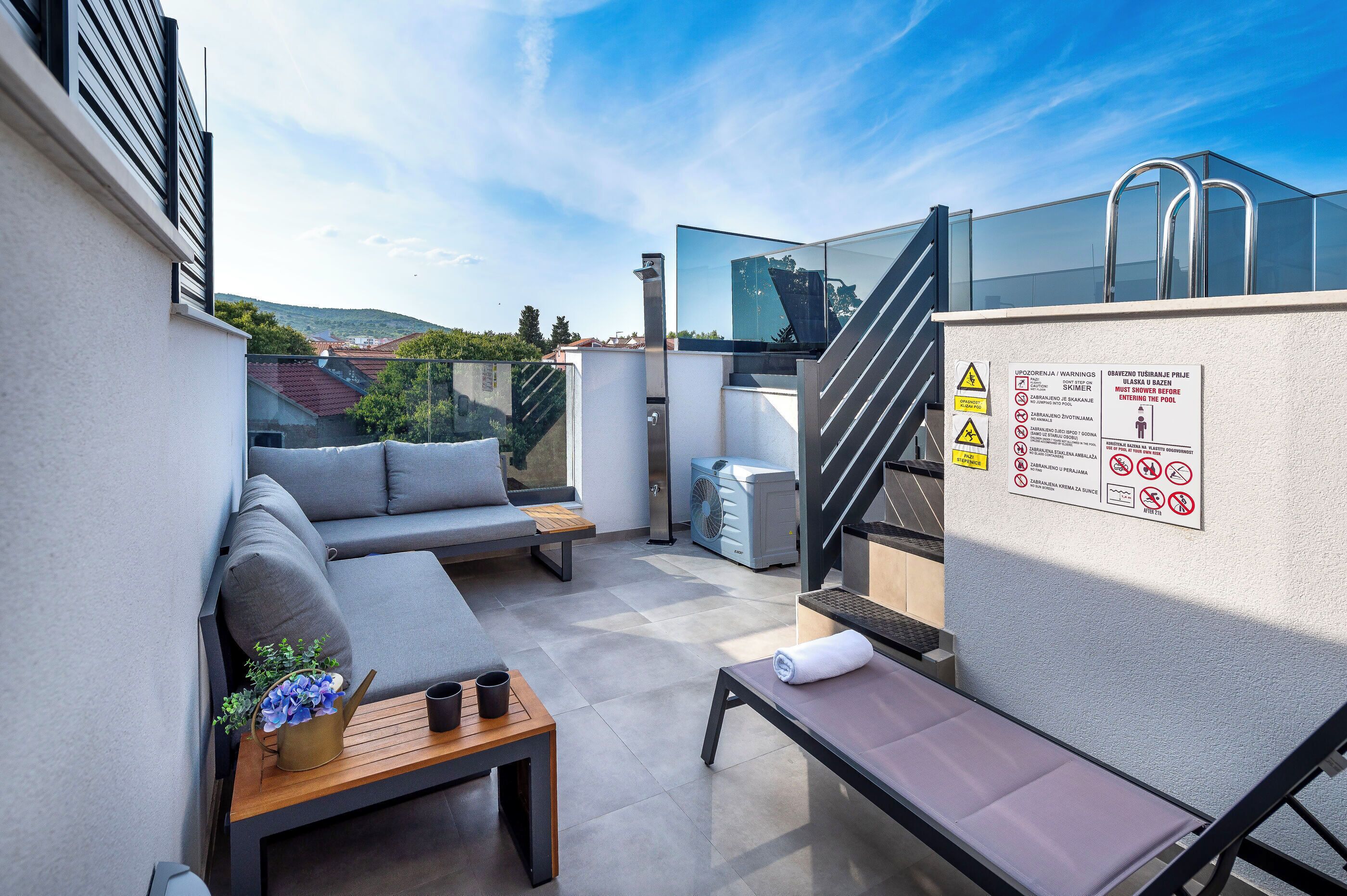 Un balcone moderno all'aperto con una divano, un tavolino con una pianta, una ventola e un asciugamano.