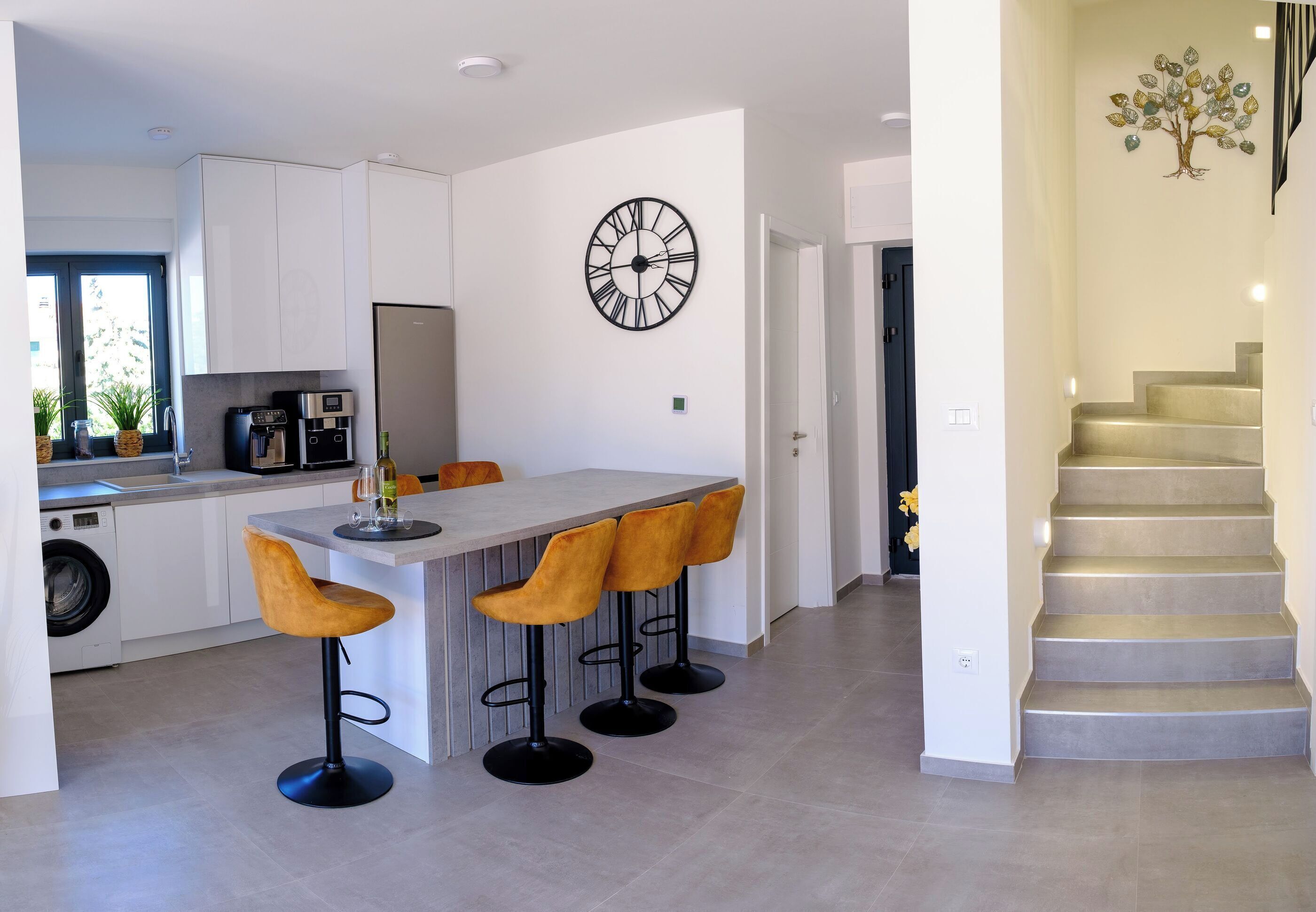 Cozinha moderna com ilha central, banquetas, relógio e escada.