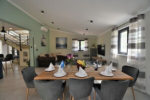 A dining area with a wooden table set for four, surrounded by grey chairs, with a staircase in the background and a TV mounted on the wall. - Villa Vala (Marcana)