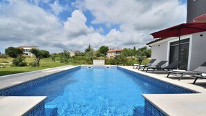 A swimming pool with tiled edges, lounge chairs, and a red umbrella. - Villa Vala (Marcana)