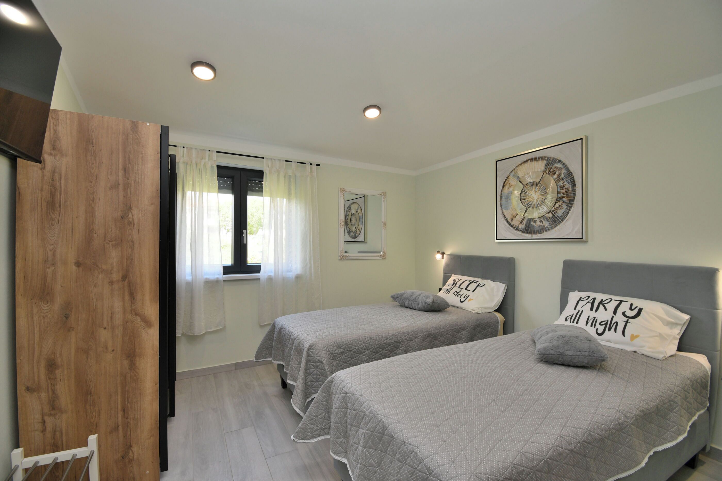 A bedroom with two beds, a wooden door, a window with curtains, and a wall with a framed picture.