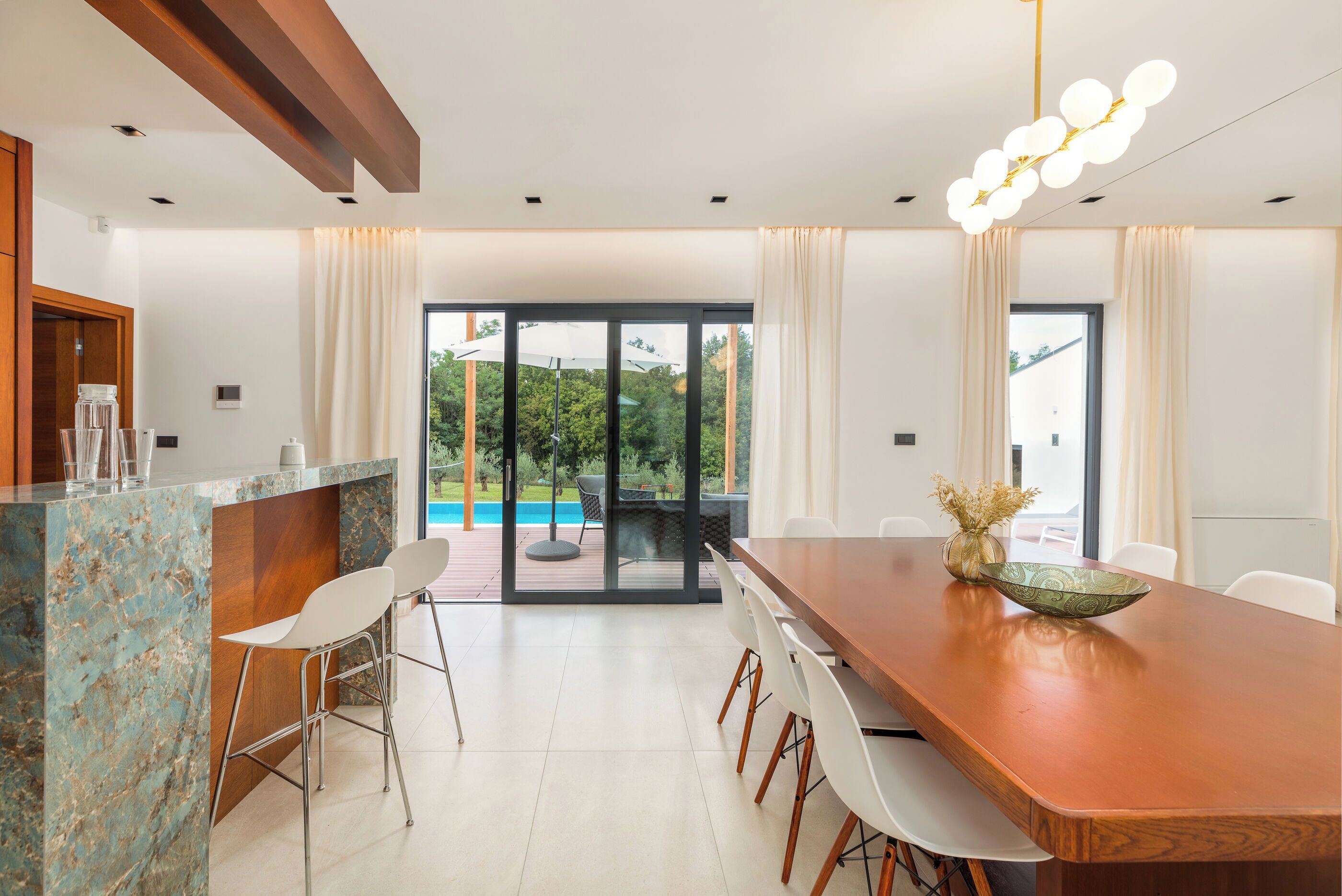 Un espace repas moderne avec une table en bois, des chaises blanches et un îlot en marbre.