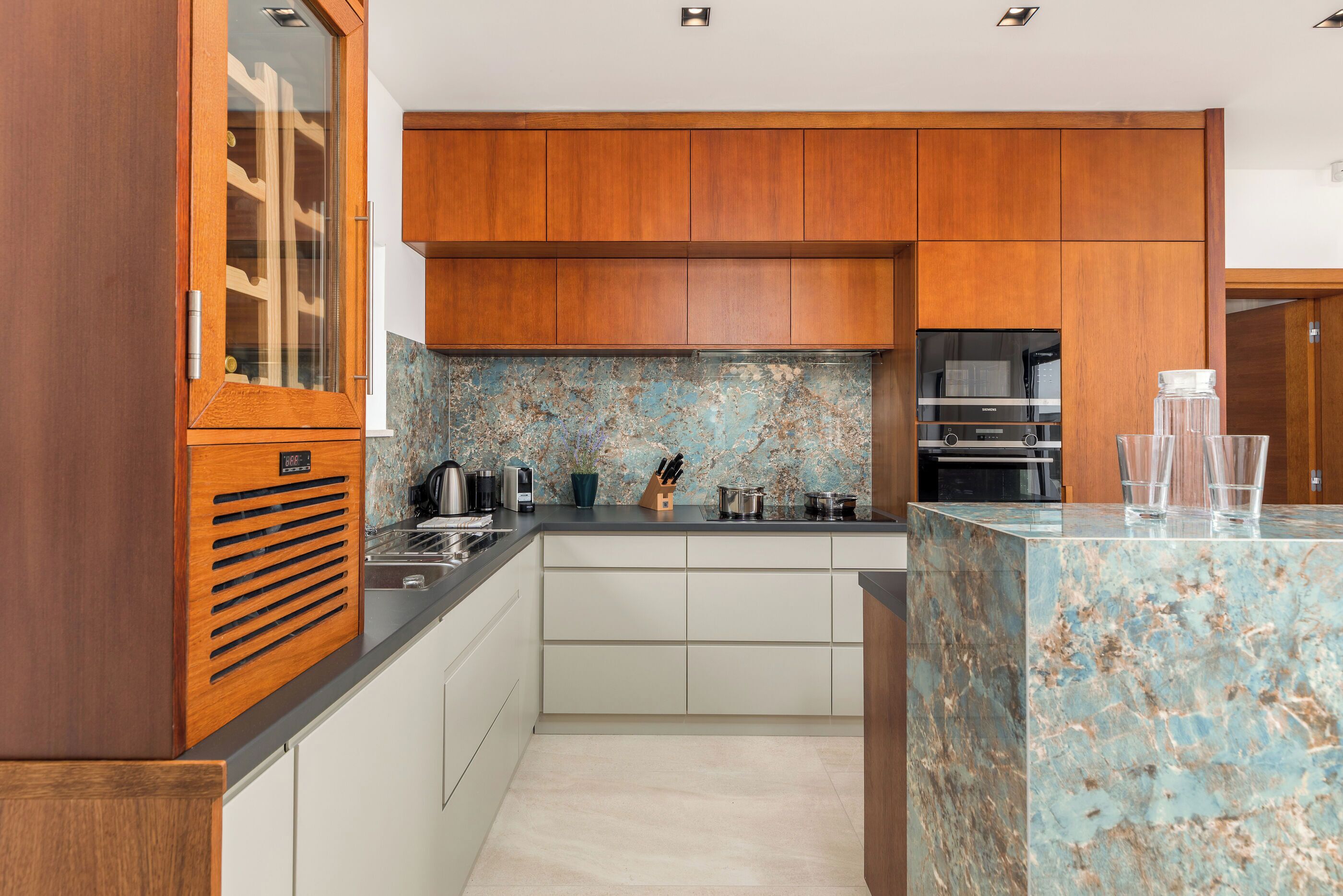 A modern kitchen with wooden cabinets, a marble countertop, and a built-in oven.
