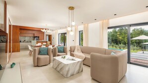 A modern living room with a marble coffee table, beige sofas, and a large window offering a view of the outdoors. - Villa Istria Green (Krsan)