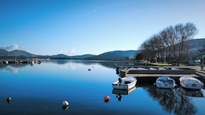 Ein ruhiger See mit anlegenden Booten, ein klarer Himmel und Berge im Hintergrund.