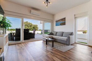 A spacious living area with a sofa, coffee table, and large windows offering a view of greenery and a body of water. - Villa Raslina Sea View (Sibenik)