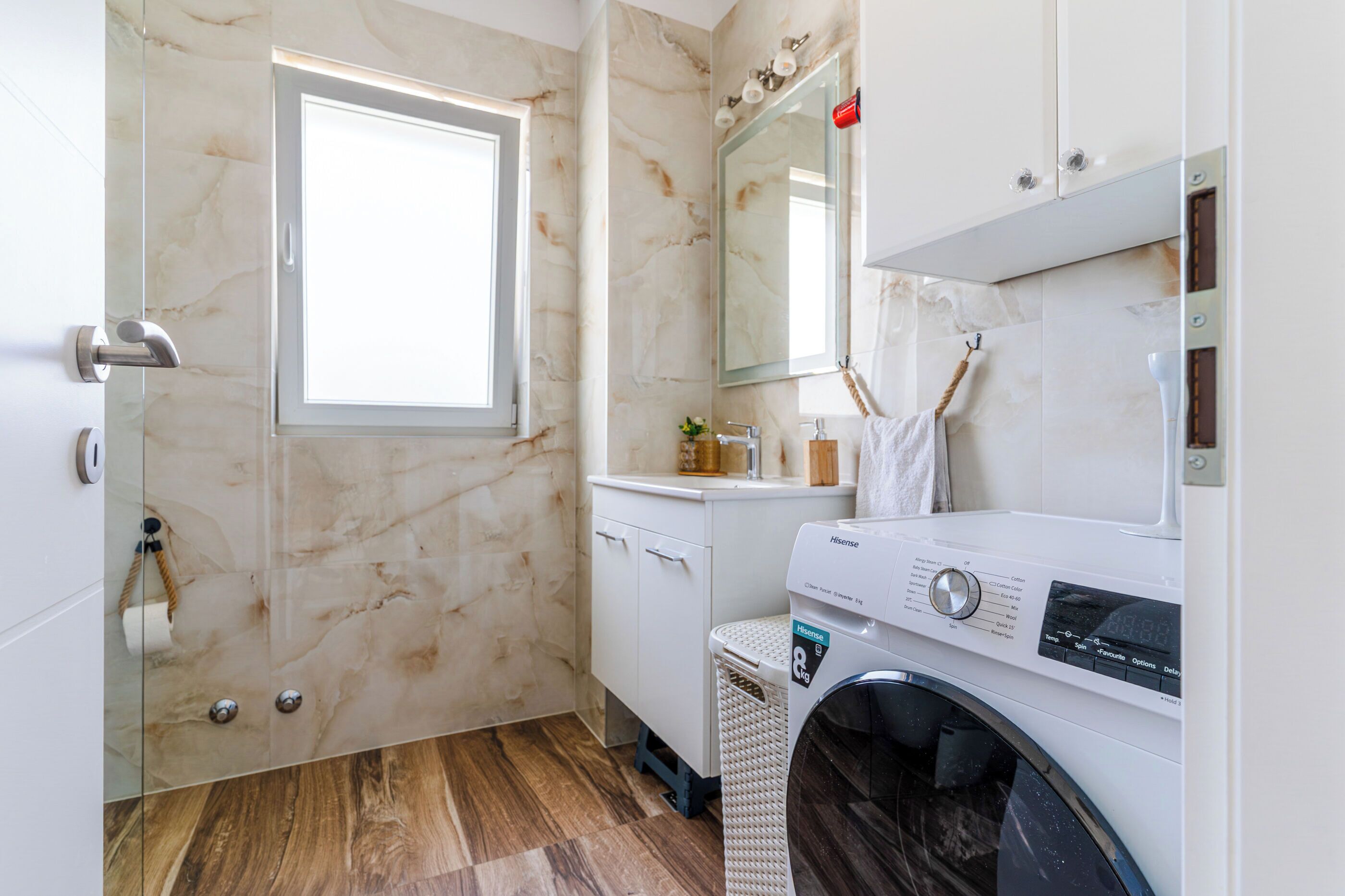 Une salle de bain moderne avec une douche à l’italienne en verre, un lave-linge encastré et un grand miroir au-dessus du lavabo.