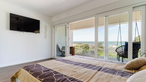 Ein Schlafzimmer mit Bett, Fernseher, einer Schiebetür zu einem Balkon und einem Sessel.