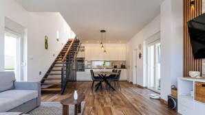 Ein modernes Wohnzimmer mit einer Couch, einem Esstisch mit Stühlen, einer Treppe und einer Küchenzeile mit Schränken und Geräten.