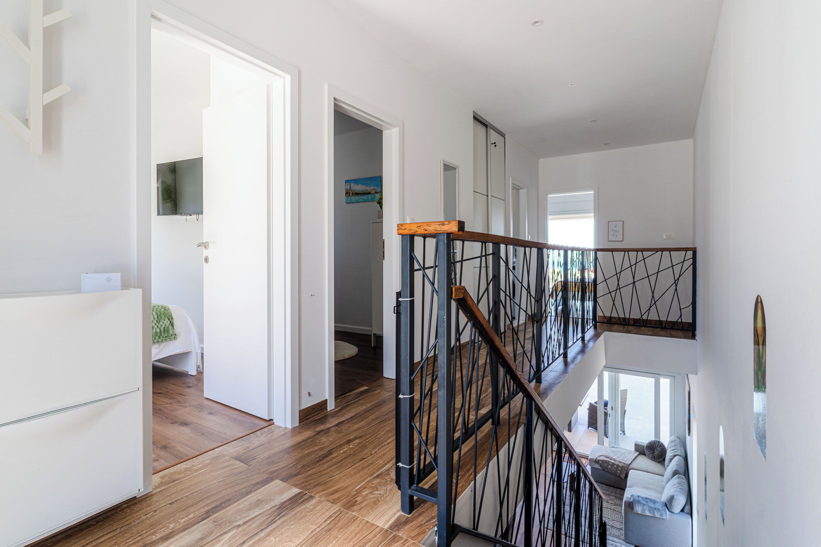 A modern interior with a wooden floor, a staircase with a metal railing, and a view of a balcony.