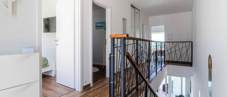A modern interior with a wooden floor, a staircase with a metal railing, and a view of a balcony.