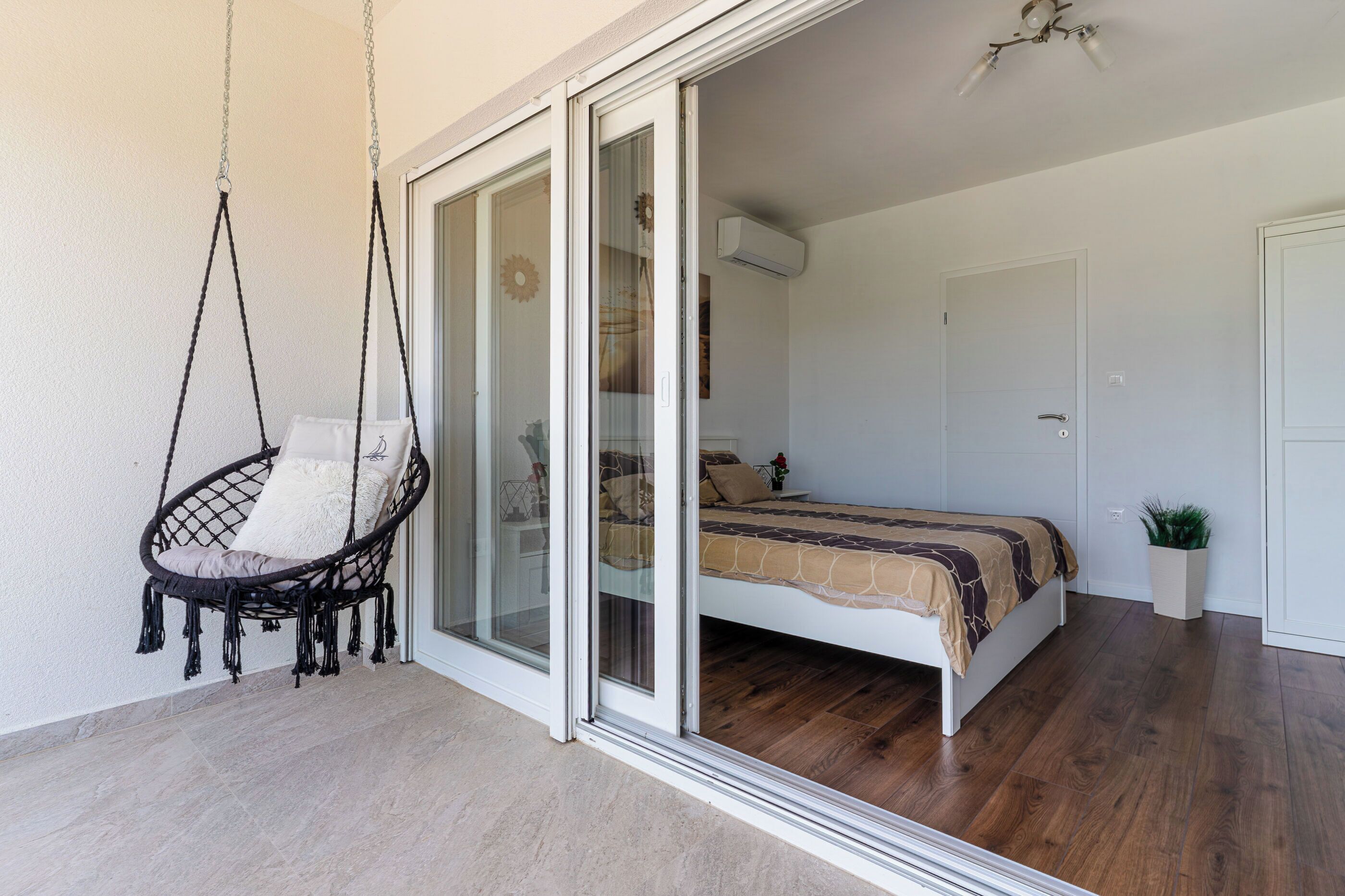 A bedroom with a bed, a hanging chair, and a sliding glass door leading to another room.