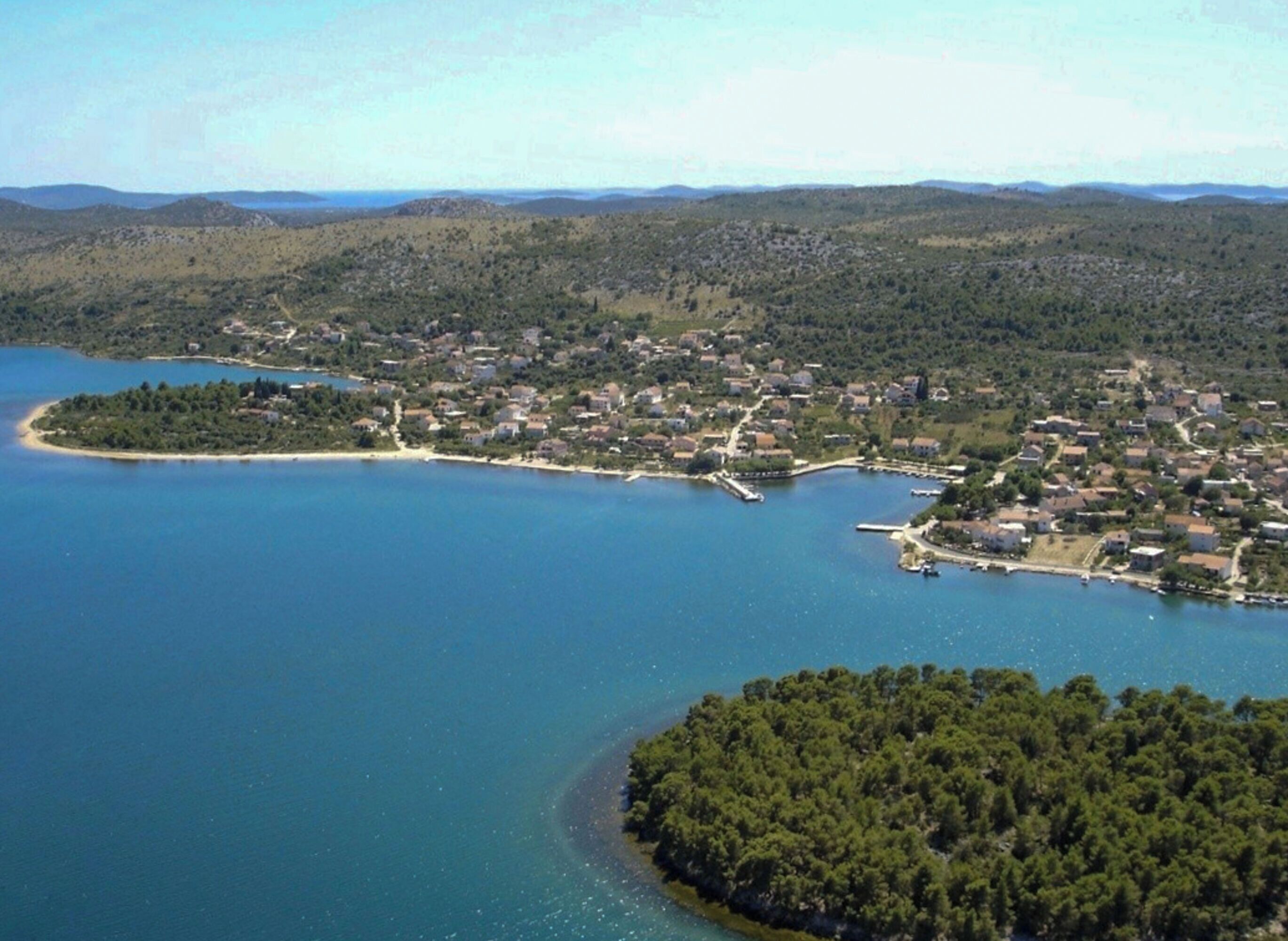 Ilmakuva rannikkokaupungista, jossa on venesatama, ja kaupunki on ympäröity kukkuloilla ja suurella vesialueella.