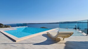 A rectangular swimming pool with clear blue water, surrounded by a tiled deck. There are lounge chairs and a glass-enclosed area with a view of the sea. - Villa Dream Come True (Jelsa)