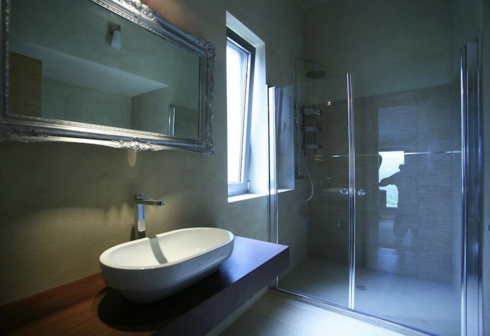 A modern bathroom with a large mirror, a vessel sink, and a glass-enclosed shower.