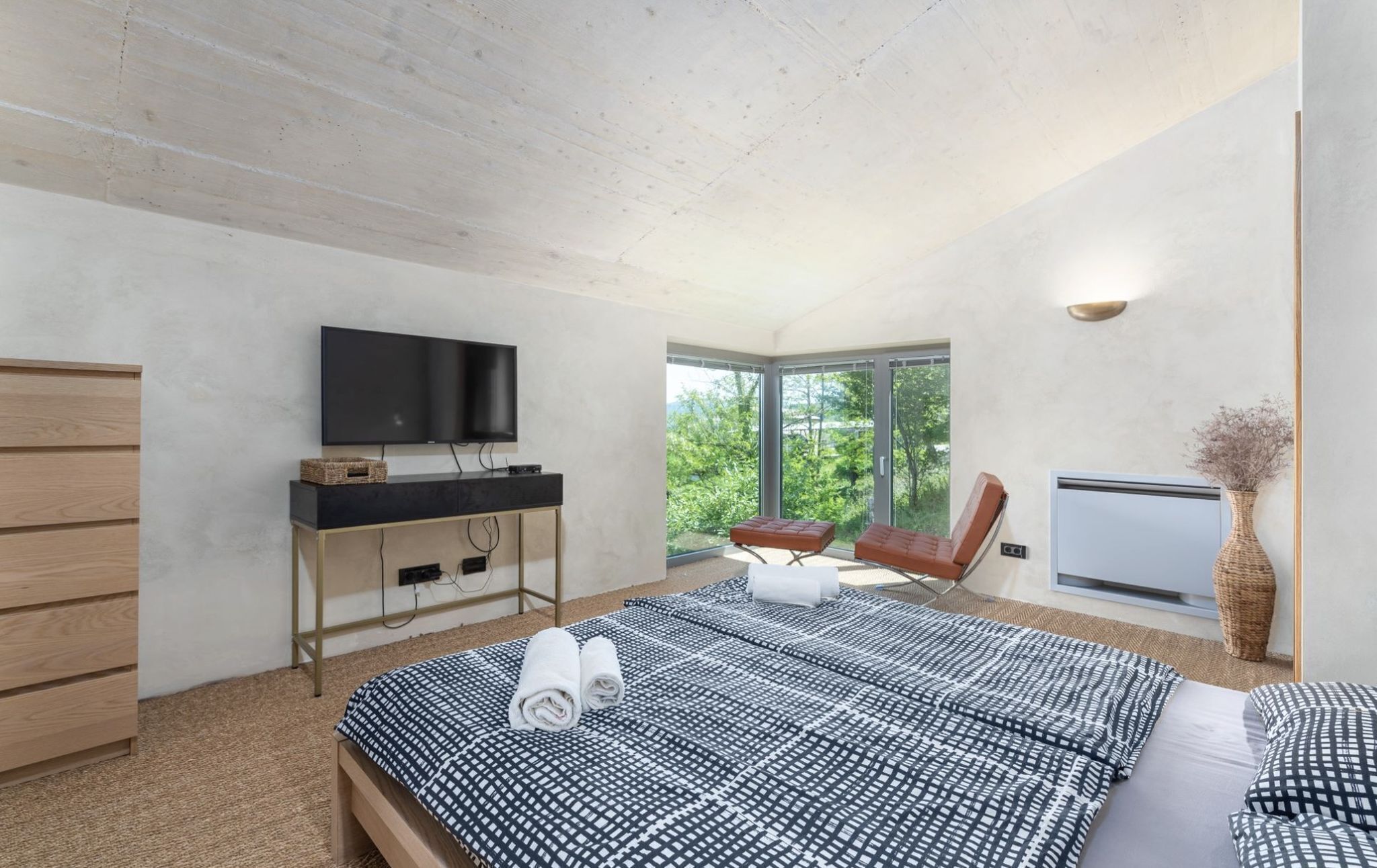 A modern bedroom with a large bed, a TV, a desk, and a chair.