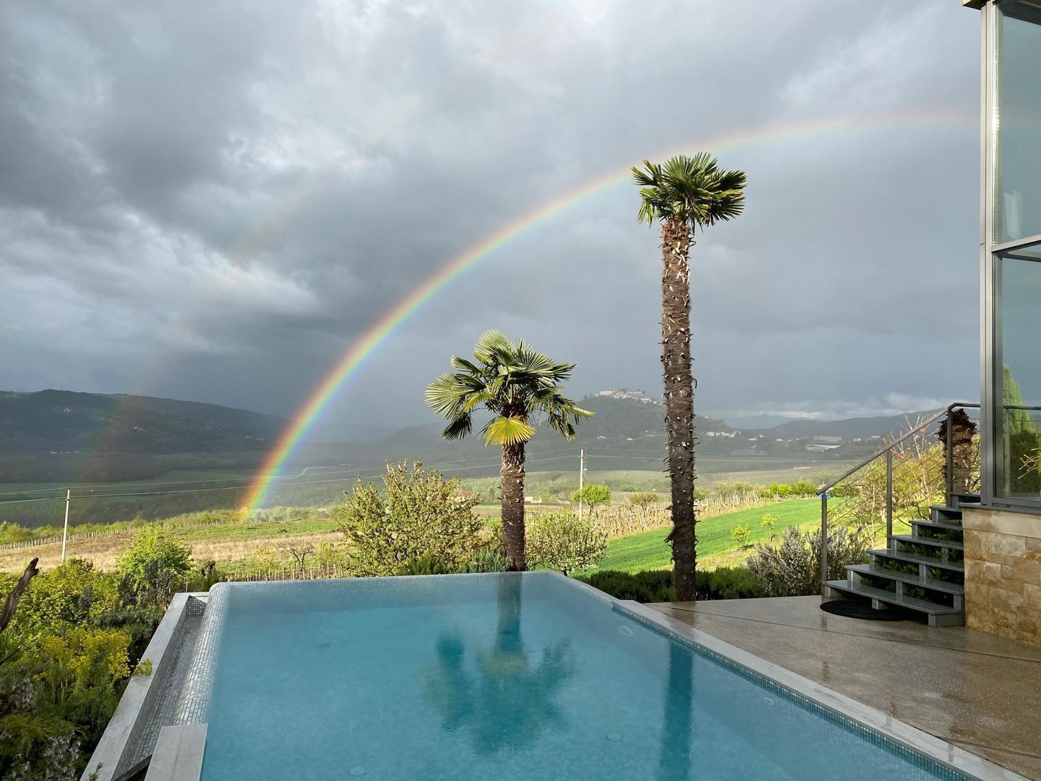 A swimming pool with a view of a rainbow, palm trees, and a distant landscape.