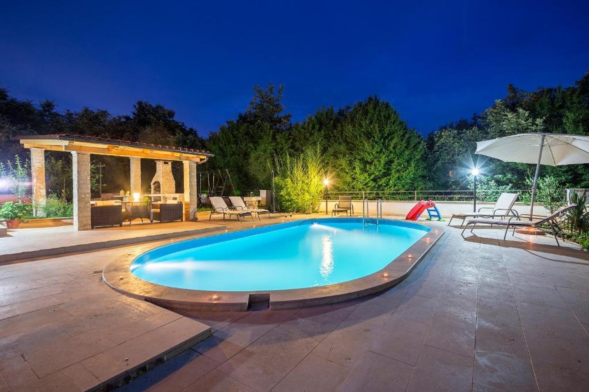 Une piscine avec des chaises longues et un espace de détente abrité, au crépuscule.