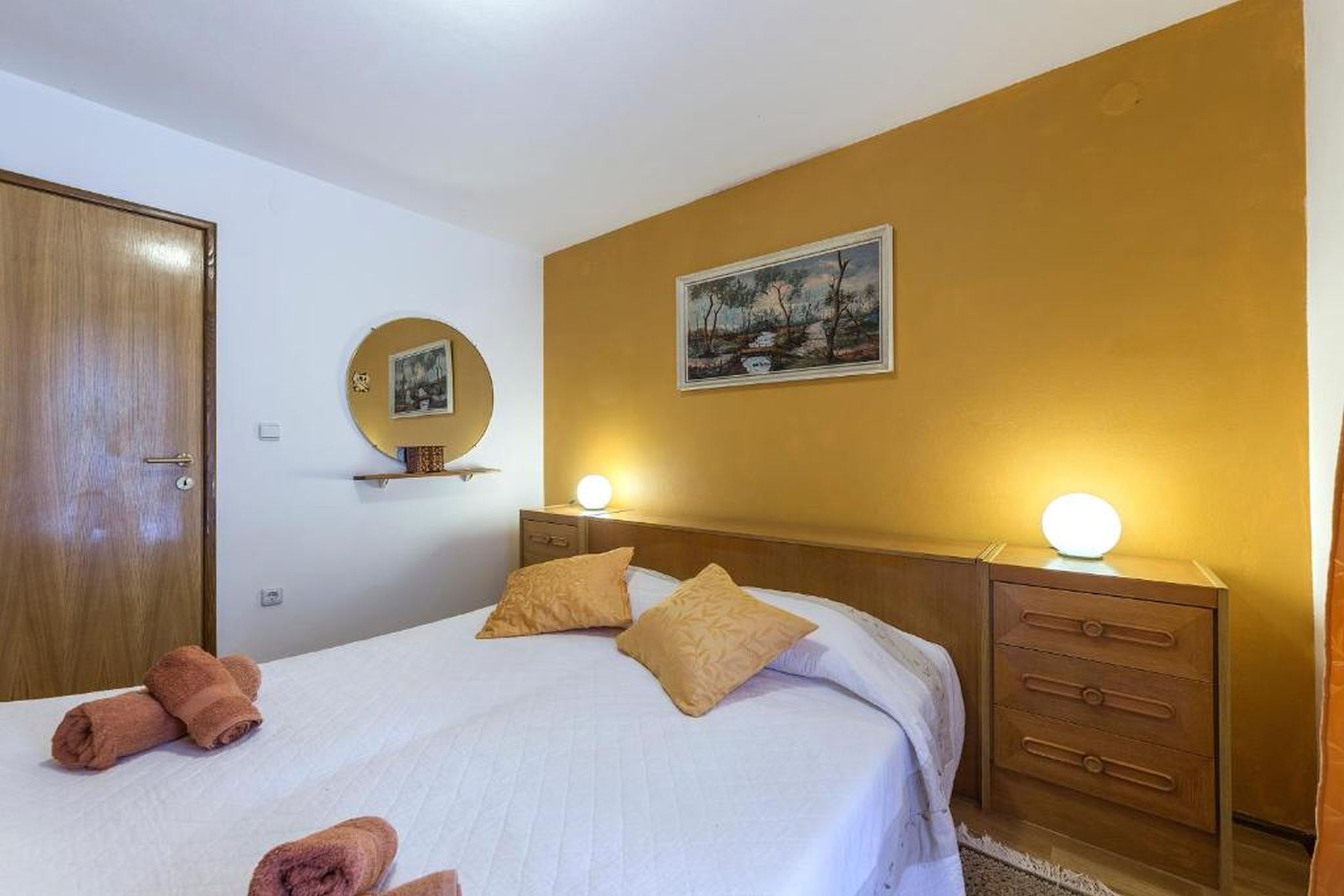 Une chambre d’hôtel comprenant un lit, une armoire en bois, une table de chevet avec une lampe et un tableau accroché au mur.