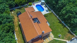 Uma casa com telhado de telhas vermelhas, piscina e quintal cercado.