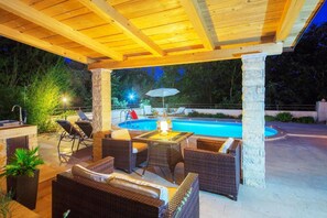 An outdoor patio with wicker furniture, a pool, and a stone pillar. - Villa Lucy (Vodnjan)