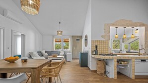 Una cucina moderna con isola centrale, zona pranzo con sedie in vimini e un soggiorno con divano.