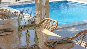 Area ristoro a bordo piscina con tavolo in legno, sottopiatti intrecciati e sedie in vimini.