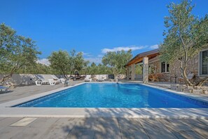 Ein Pool mit Liegestühlen, ein Steinhaus und Bäume.