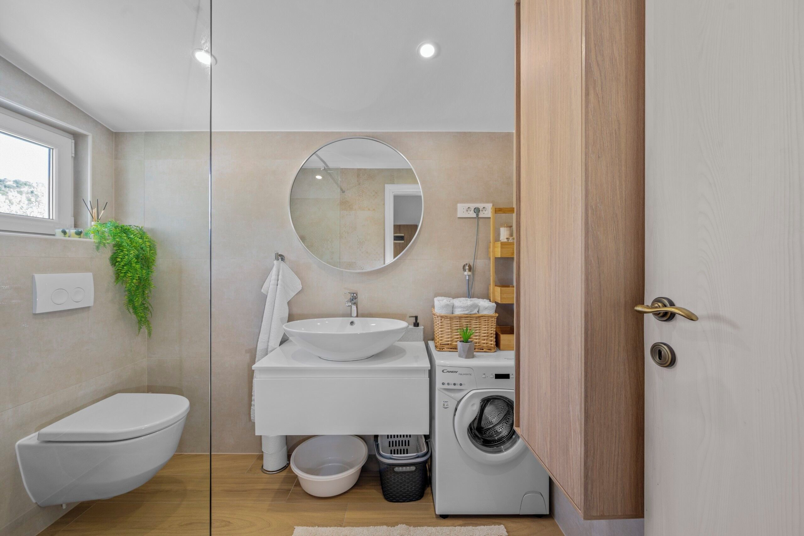 Een moderne badkamer met toilet, wastafel, spiegel en wasmachine.