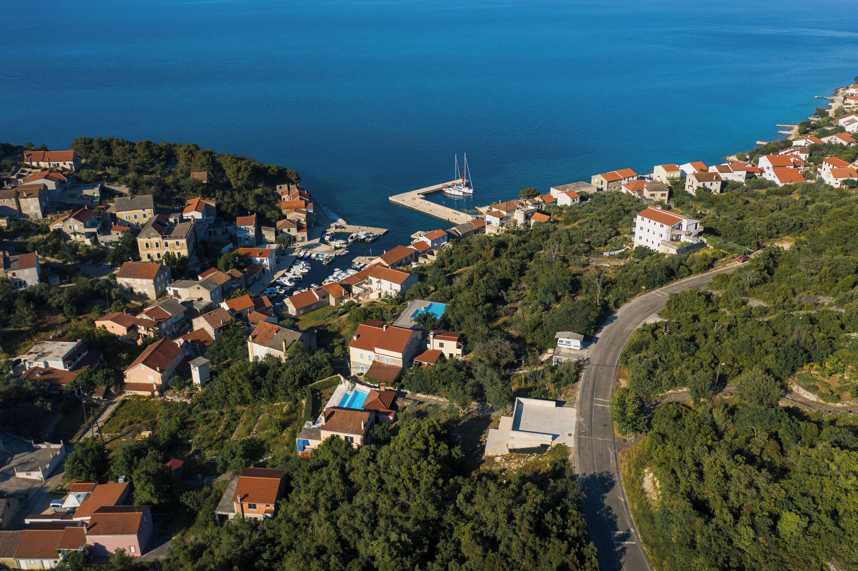 An aerial view of a coastal town with houses, a marina, and a road curving through the landscape.
