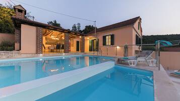 Una piscina con un porche techado, mobiliario exterior y vistas del paisaje circundante.