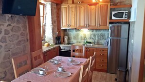 A cozy kitchen with wooden cabinets, a dining table set with plates and cups, a microwave, and a refrigerator. - Villa Peace (Dugi Rat)