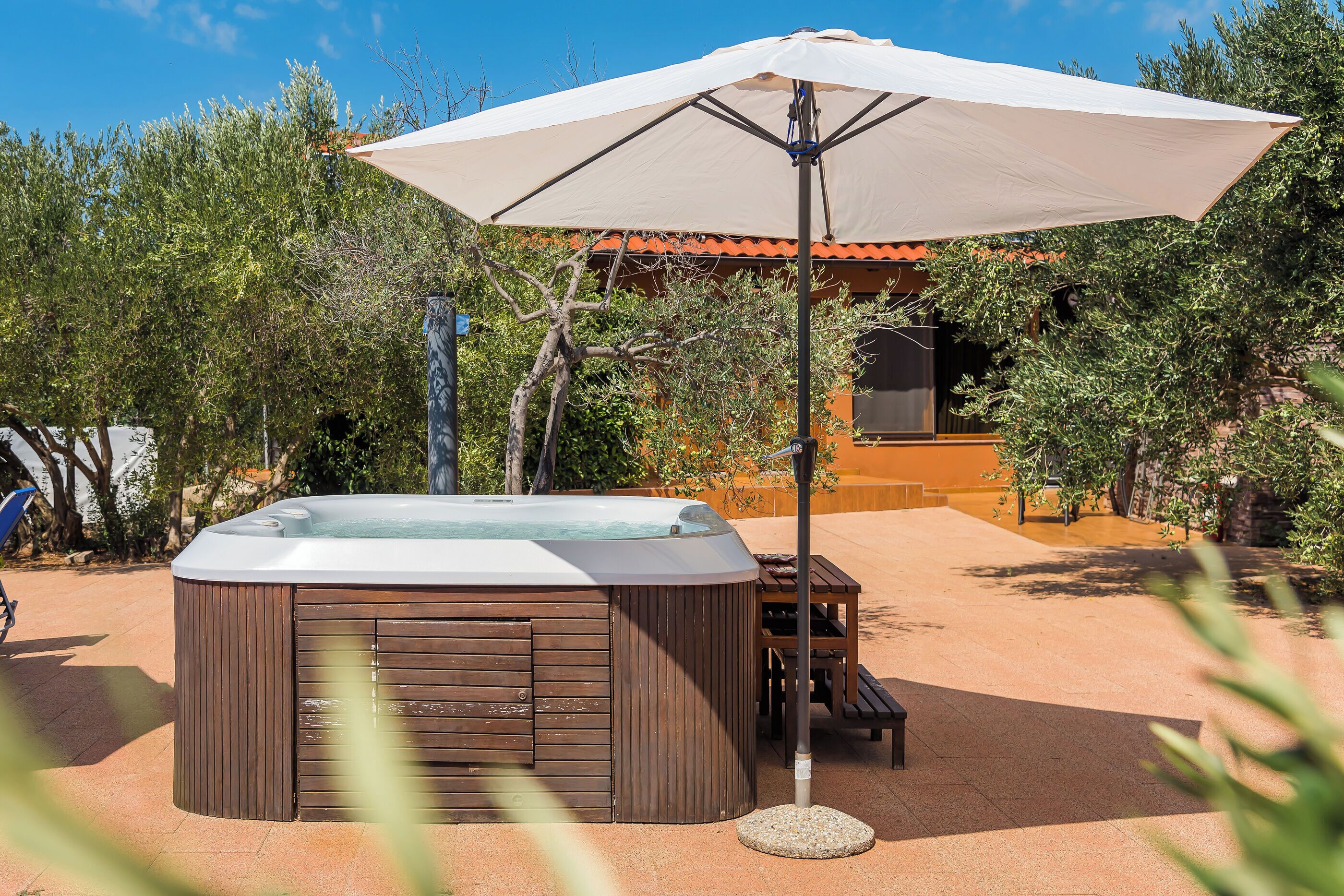A hot tub with a wooden exterior, an umbrella, and a patio table.