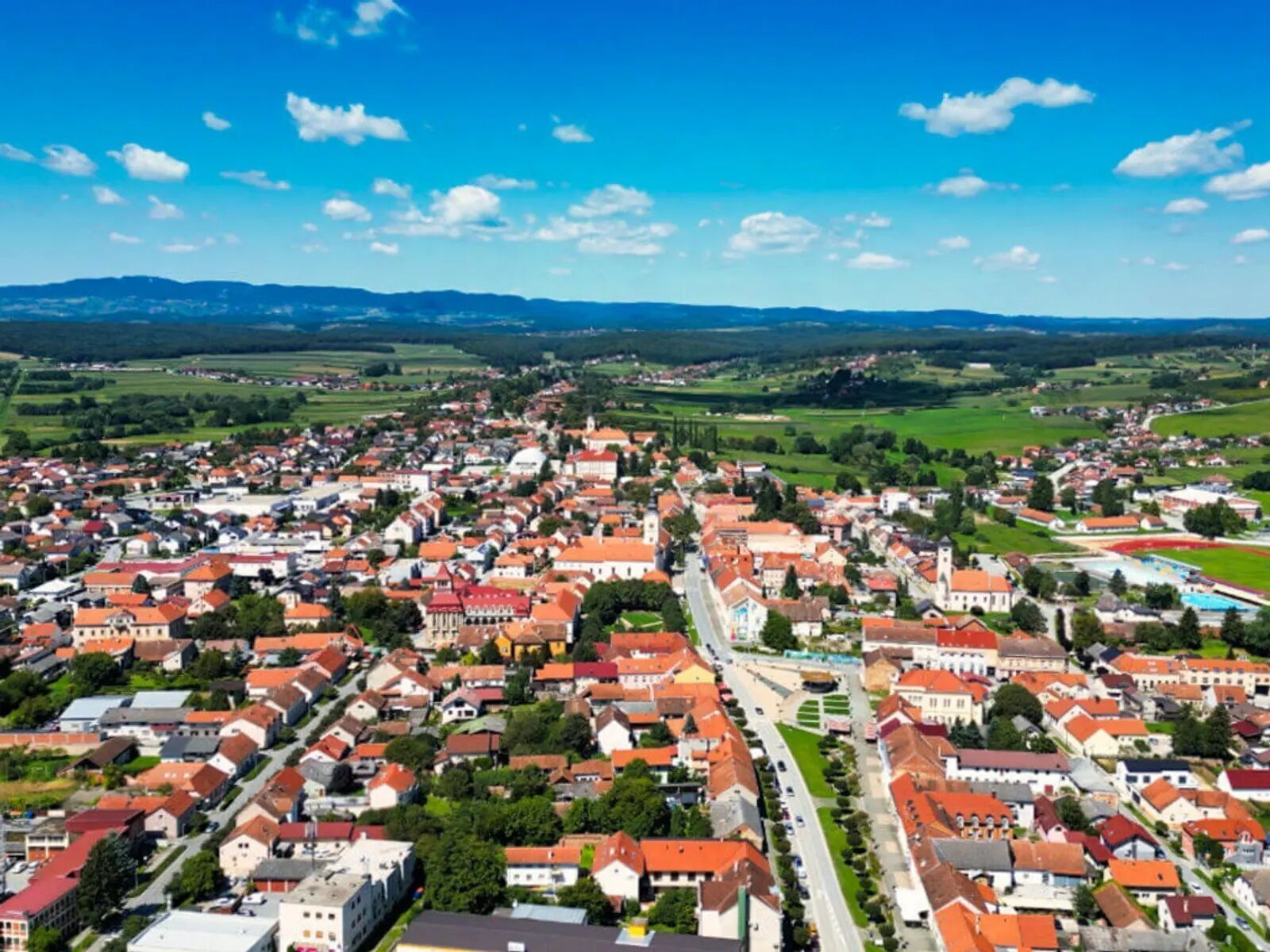 A town with red-roofed buildings, a central road, and surrounding green fields.