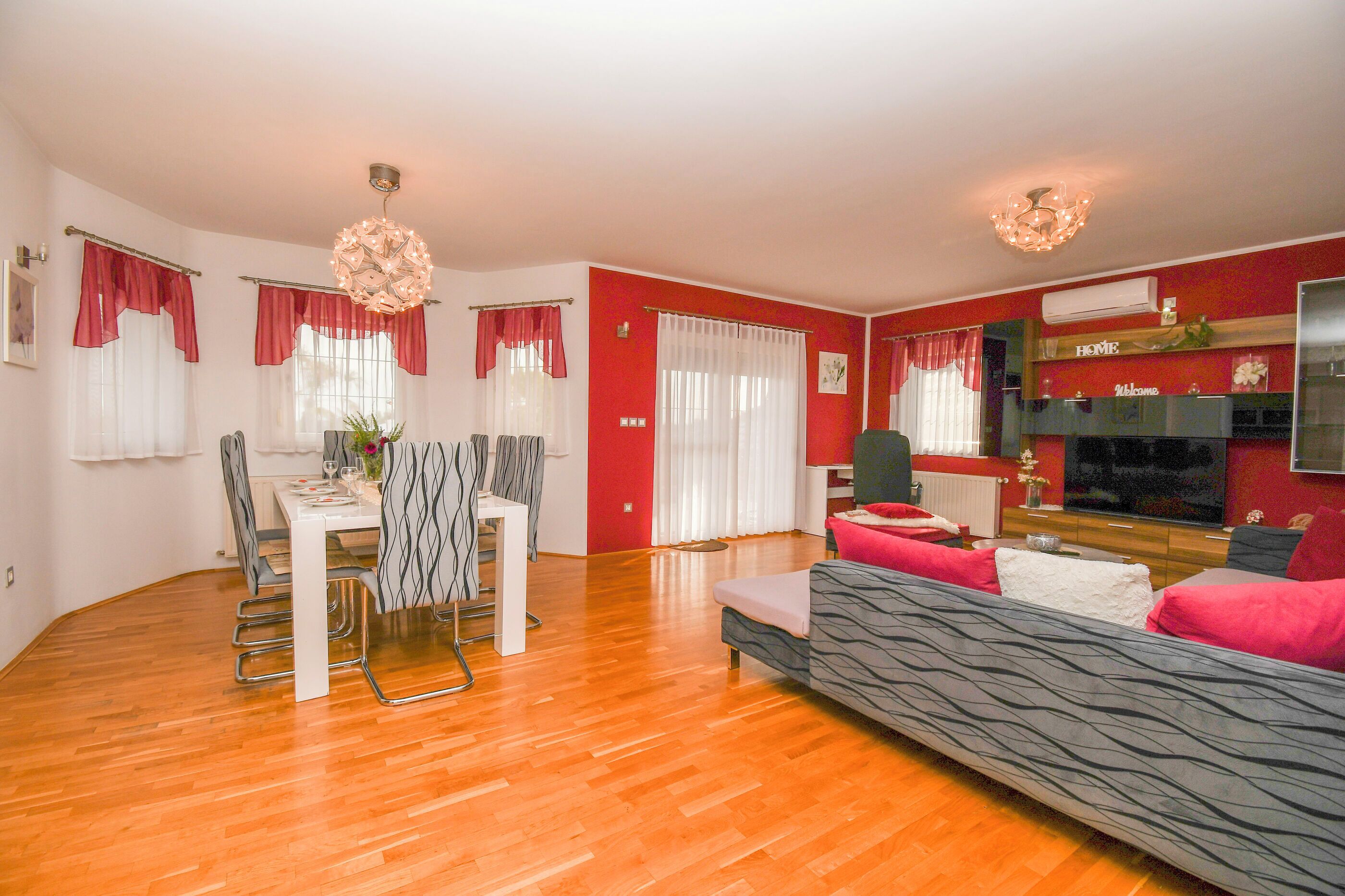 Un salon comprenant un coin repas, avec des murs rouges, un parquet en bois et un lustre moderne.