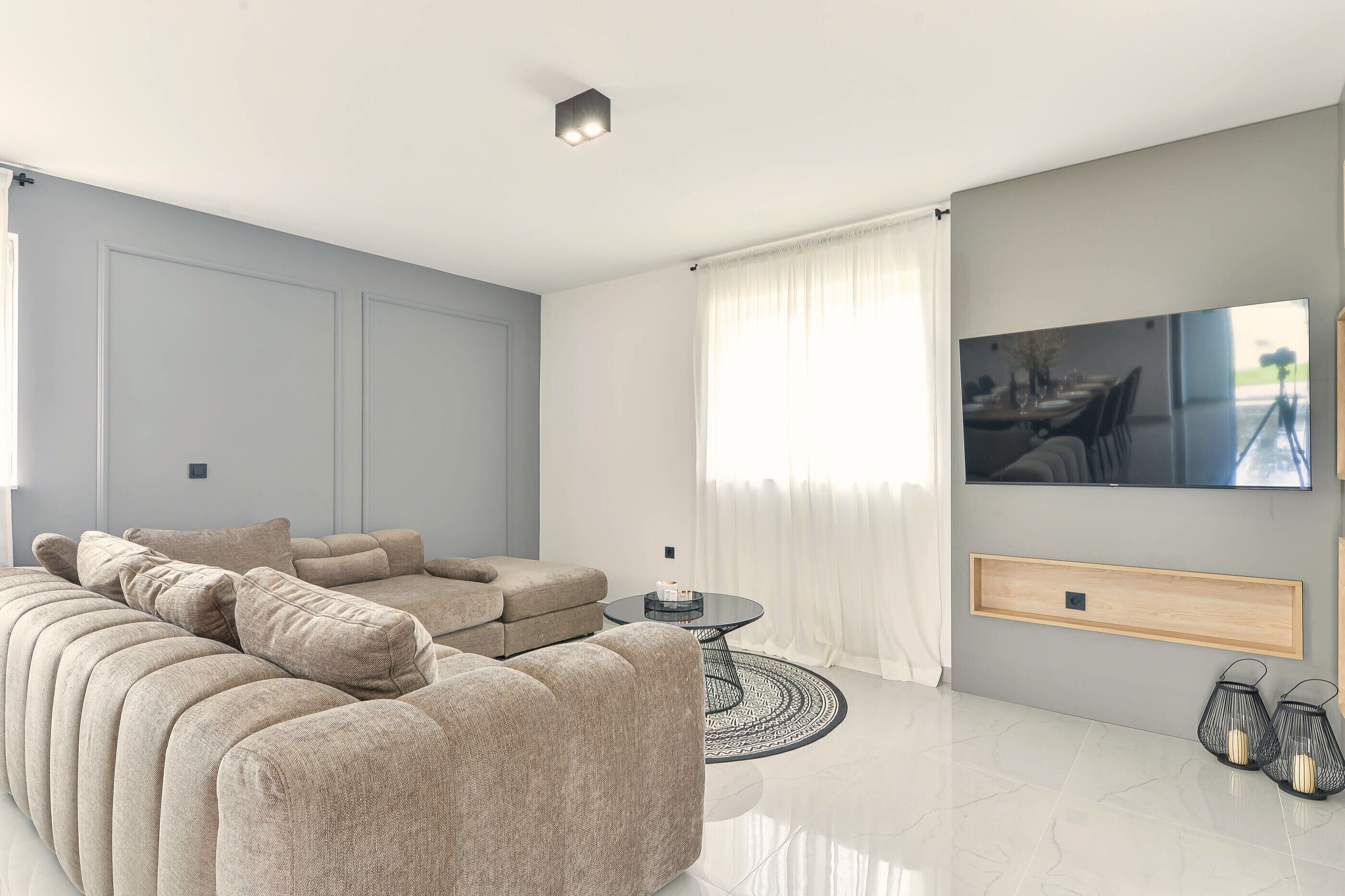 A modern living room with a sectional sofa, a round coffee table, and a flat-screen TV mounted on the wall.