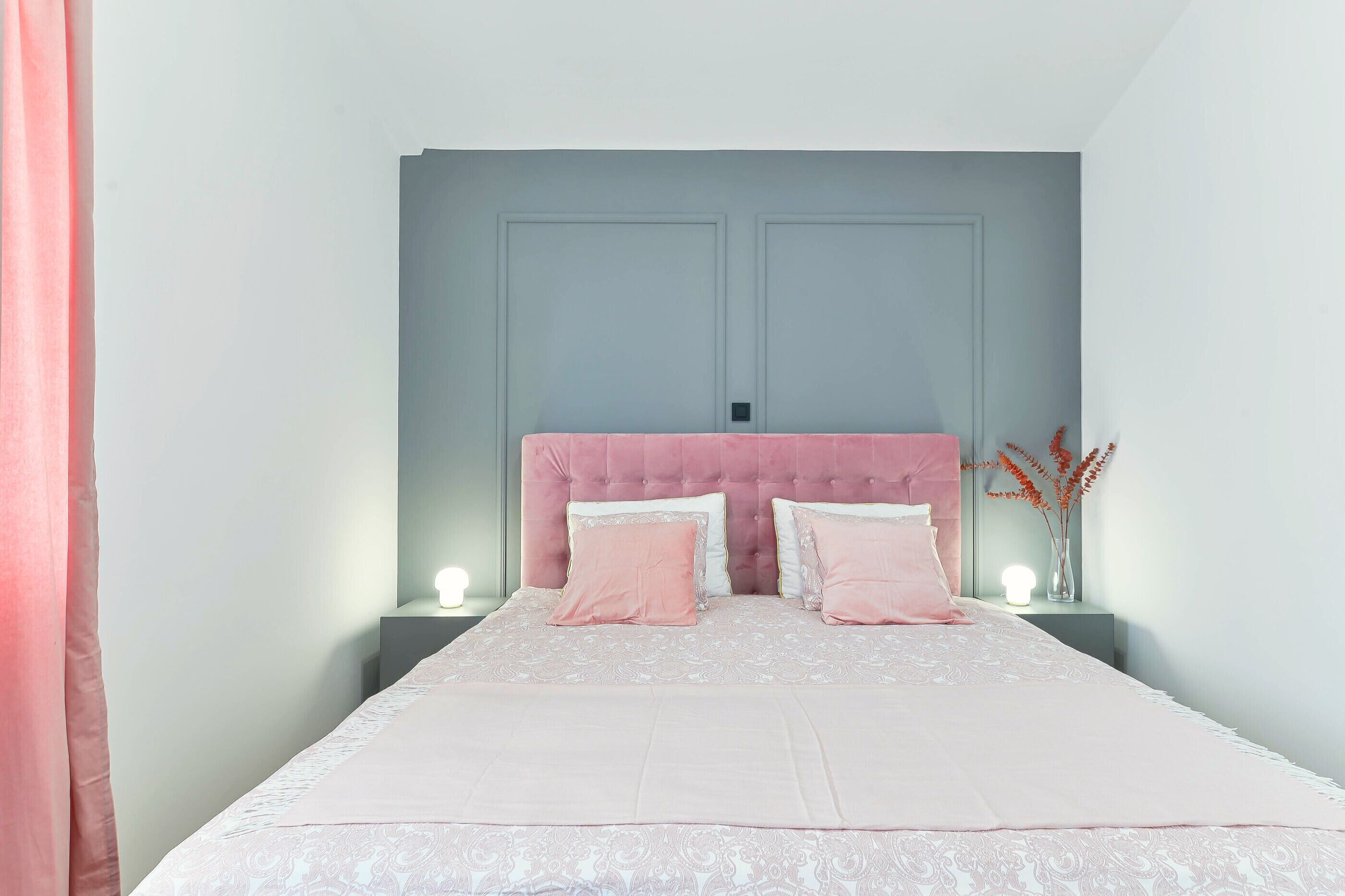 Un dormitorio con una cama, dos mesitas de noche, una lámpara de pared y un florero con flores secas.