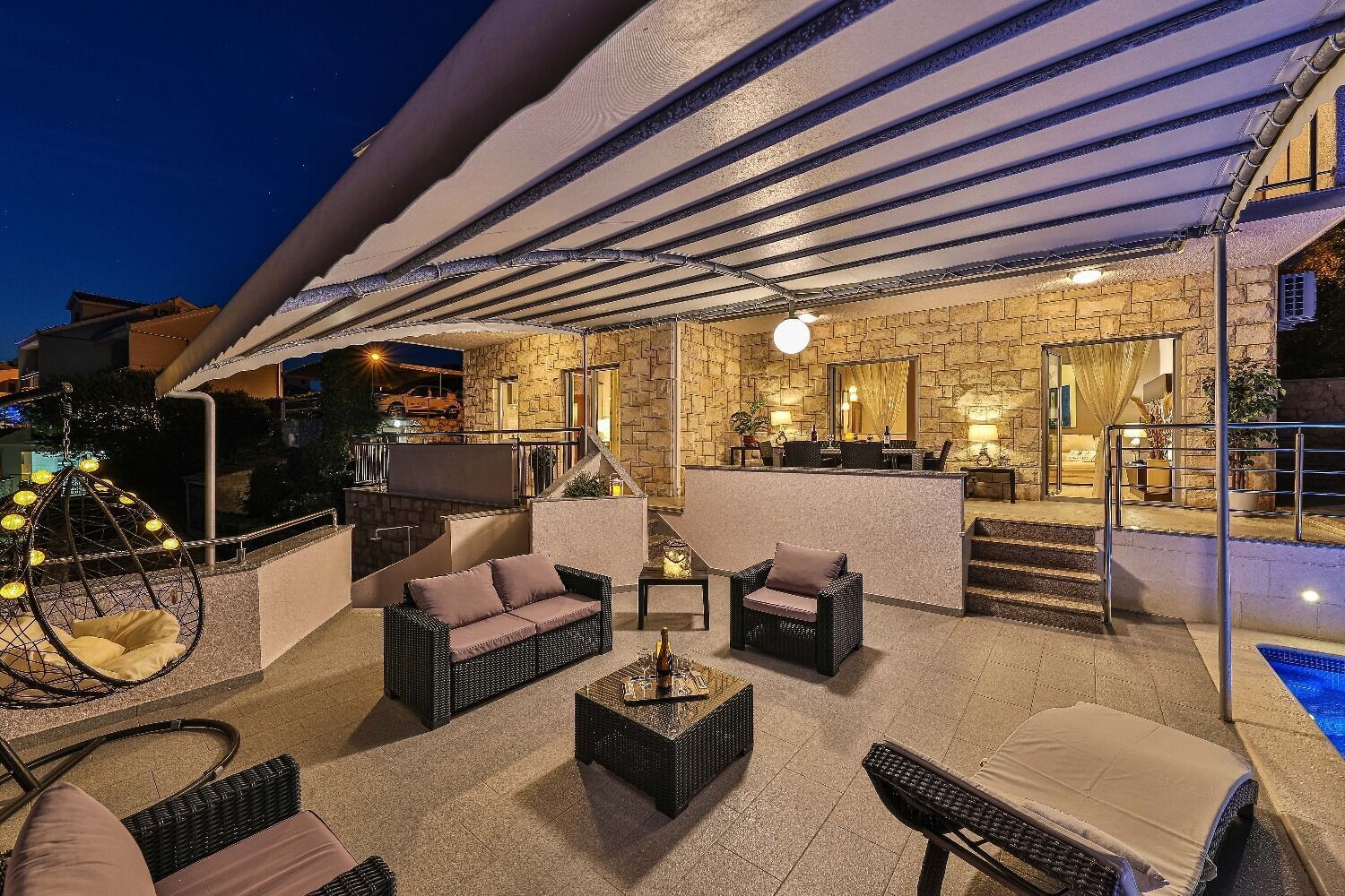An outdoor patio area with wicker furniture, a hanging light fixture, and a stone wall backdrop.