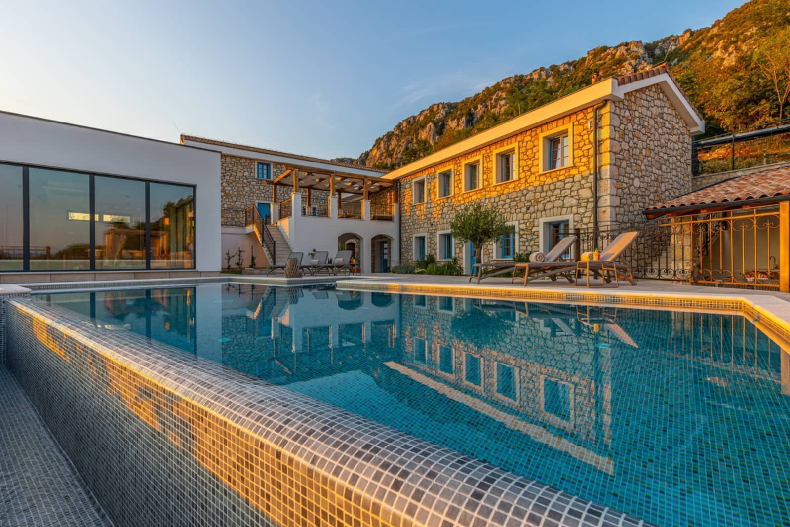 Ein moderner Poolbereich mit einem Steinhaus, einer Glasfassade und Blick auf eine Berglandschaft.