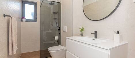 Un baño moderno con cabina de ducha de vidrio, un lavabo blanco con espejo y suelo de madera.