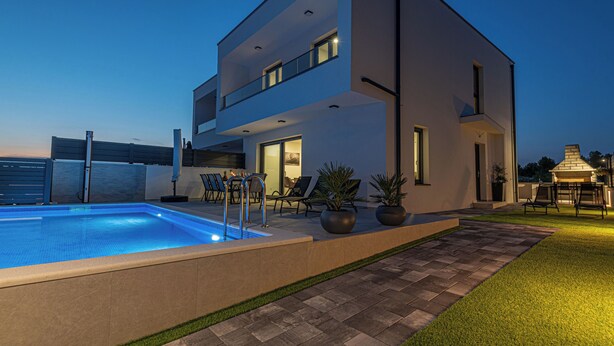 Una casa moderna de dos pisos con piscina, mobiliario exterior y zona de barbacoa.