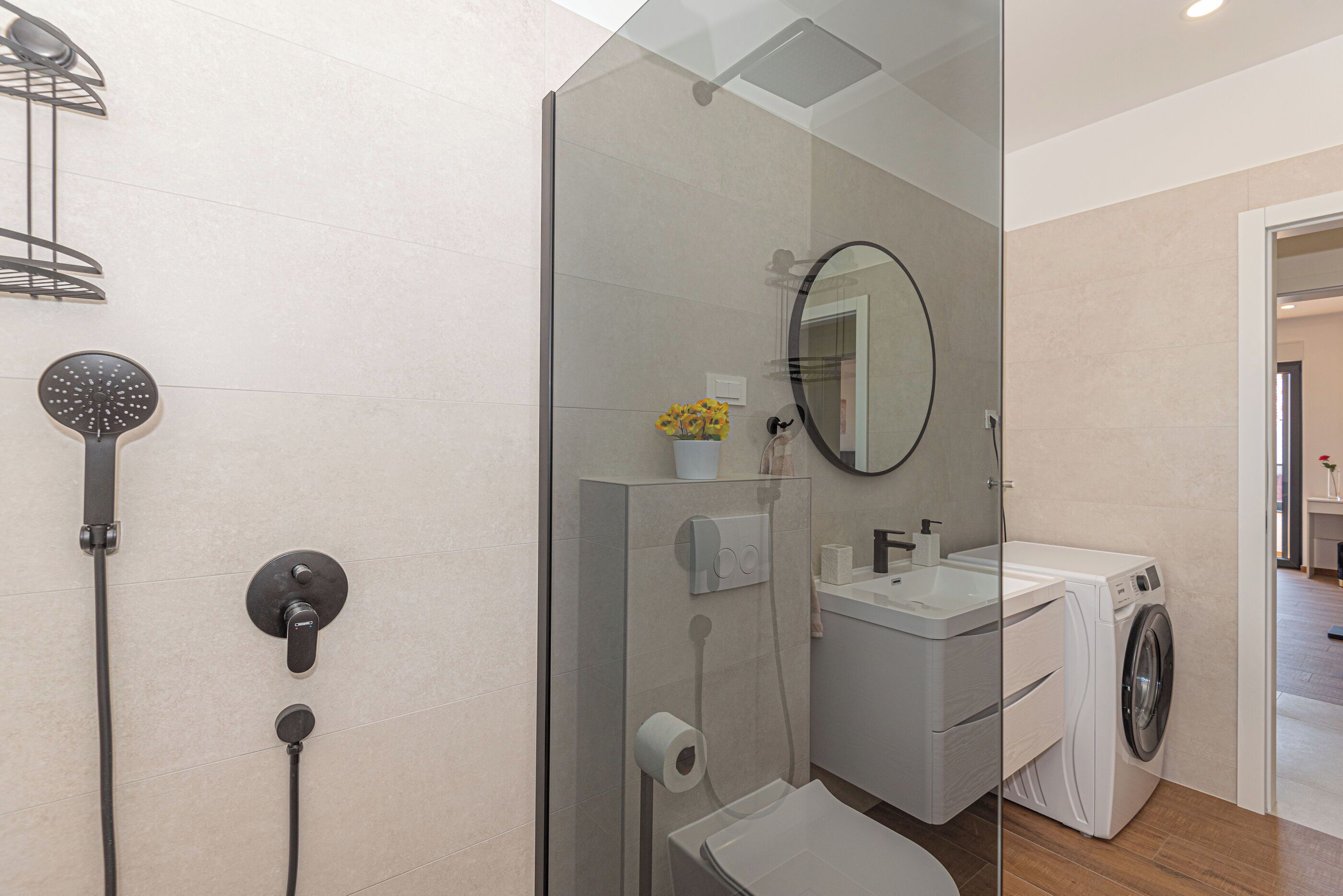 Un bagno moderno con box doccia in vetro, un water, un lavandino e una lavatrice.