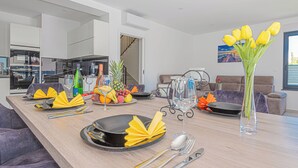 Un comedor moderno con una larga mesa dispuesta para una comida, con servilletas amarillas, platos negros y un jarrón con flores amarillas.