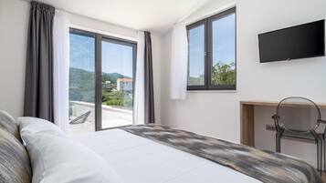 A hotel room with a bed, a desk, a chair, a TV, and large windows with curtains.