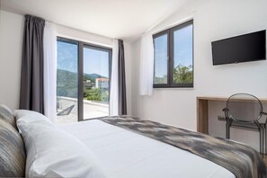 A hotel room with a bed, a desk, a chair, a TV, and large windows with curtains. - Villa Eden With Heated Pool (Omis)