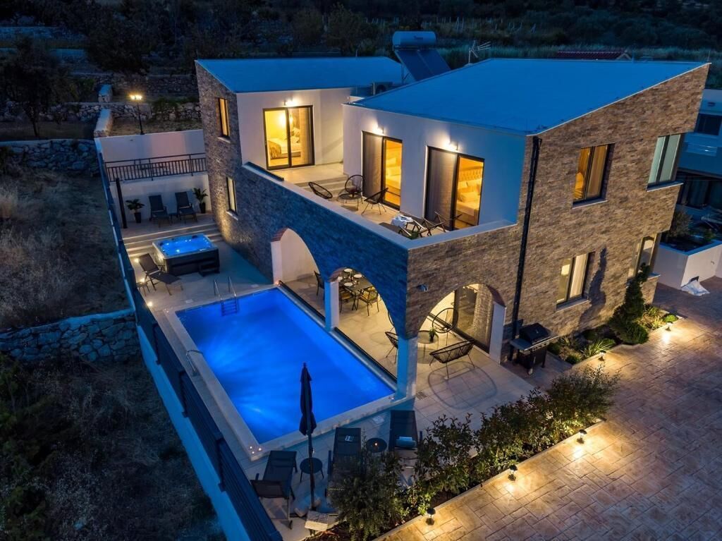 A modern two-story house with a swimming pool, outdoor seating, and a stone facade.