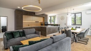 A modern kitchen with a central island, grey sofas, and a dining area with a wooden table and chairs. - Villa Eden With Heated Pool (Omis)