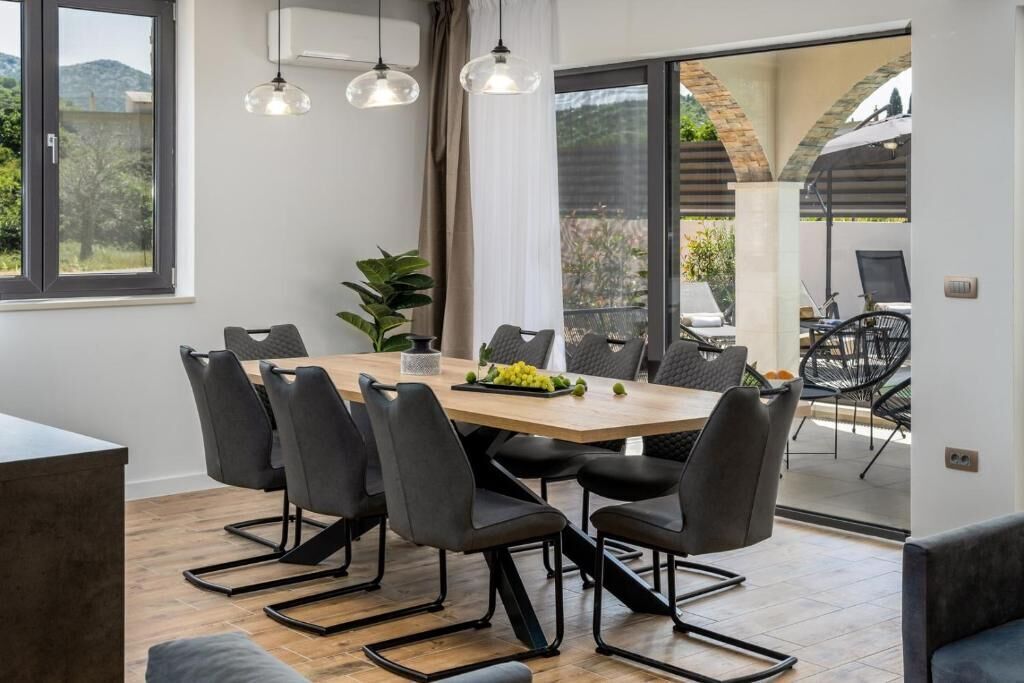 Un comedor moderno con una mesa de madera y sillas negras, una planta en maceta y vistas a un patio exterior con sillas y una mesa.
