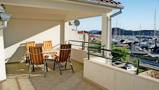 Ein Balkon mit zwei Stühlen und einem Tisch, mit Blick auf einen Jachthafen mit Booten und einer hügeligen Landschaft.